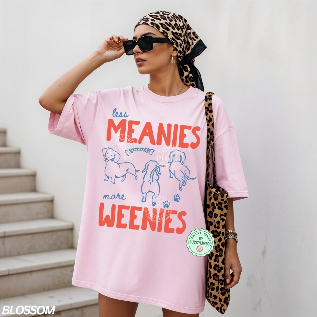 Person wearing a pink t-shirt with dachshund  graphics and text saying ‘less meanies, more weenies’ standing on a street.